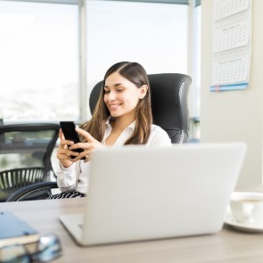 Woman sitting at desk looking with cell phone in hand | Sun-Surf Realty Emerald Isle NC