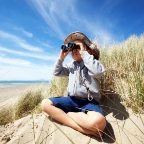 Boy looking through binoculars on Emerald Isle beach | Sun-Surf Vacation Rentals Emerald Isle, NC